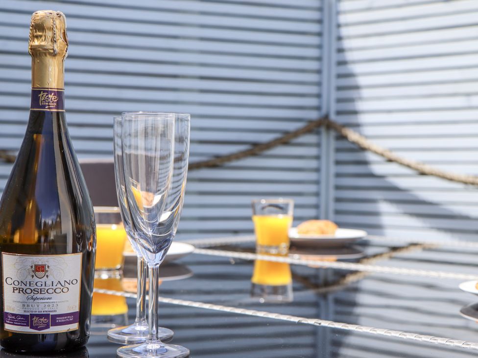 An outdoor dining area with a bottle of Prosecco and glasses at Driftwood in Torquay