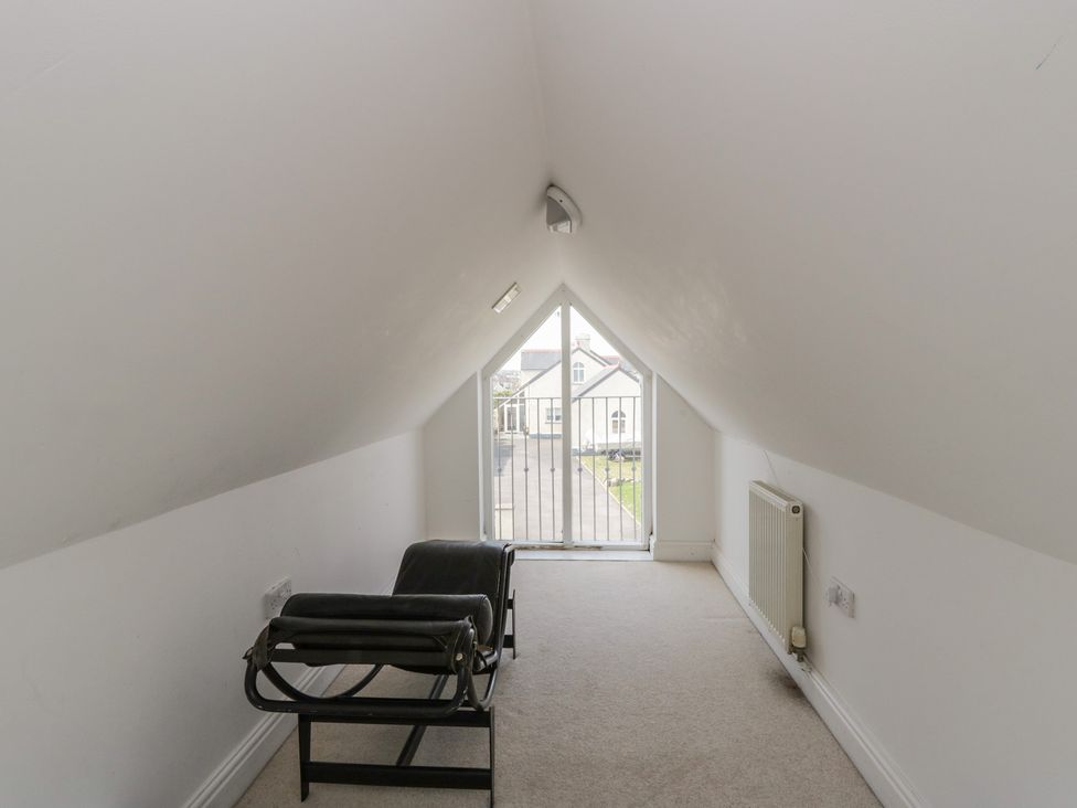 A loft space with a chair and a view to a balcony at Awen Ingli, Newport, Pembrokeshire