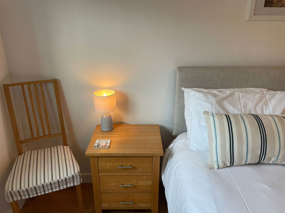 A bedroom with a bed, nightstand, lamp, chair and booklet at Broadleys in Swanage