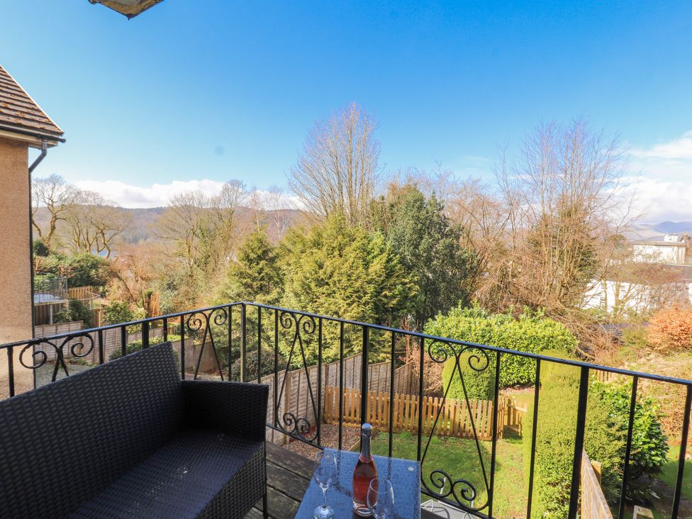 A balcony with a bottle and glasses overlooking a garden at Lake View in Bowness-On-Windermere