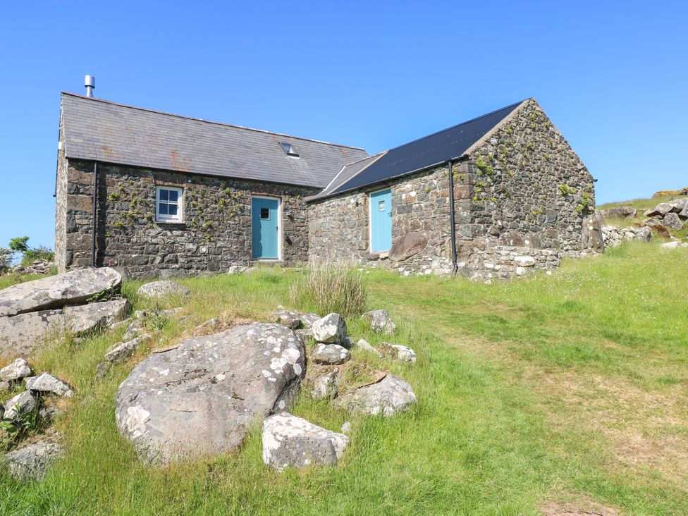 A stone cottage with blue doors and a grassy area with rocks at Ty Mellen in Dinas Cross