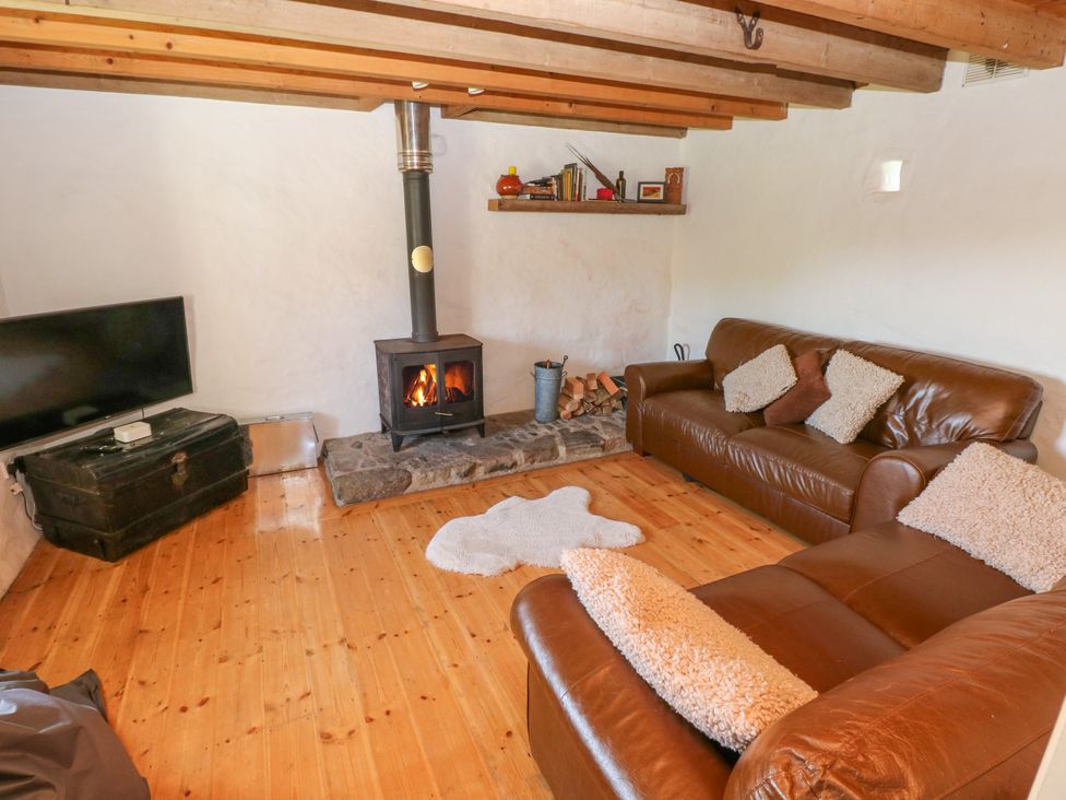 A living room with a wood stove fireplace two brown leather sofas a flat screen TV and a wooden floor at Ty Mellen in Dinas Cross