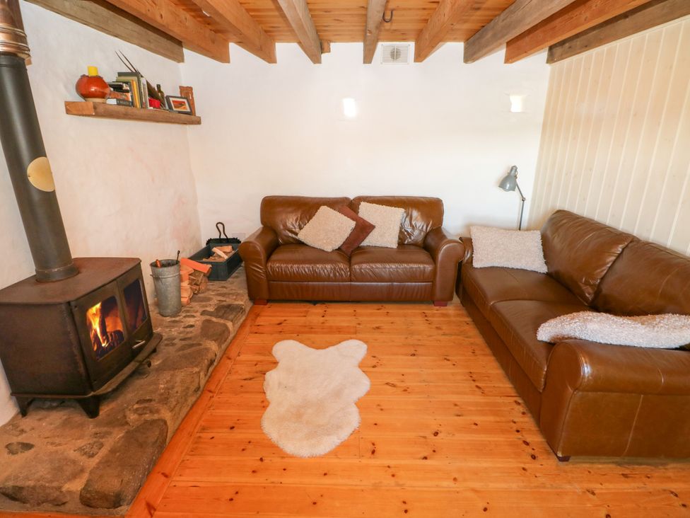 A living room with two brown leather sofas a wood burning stove and a small rug on the floor at Ty Mellen in Dinas Cross