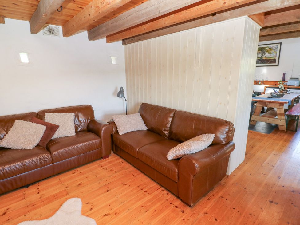 A living room with two brown leather sofas and cushions next to a wooden wall and visible dining table at Ty Mellen in Dinas Cross