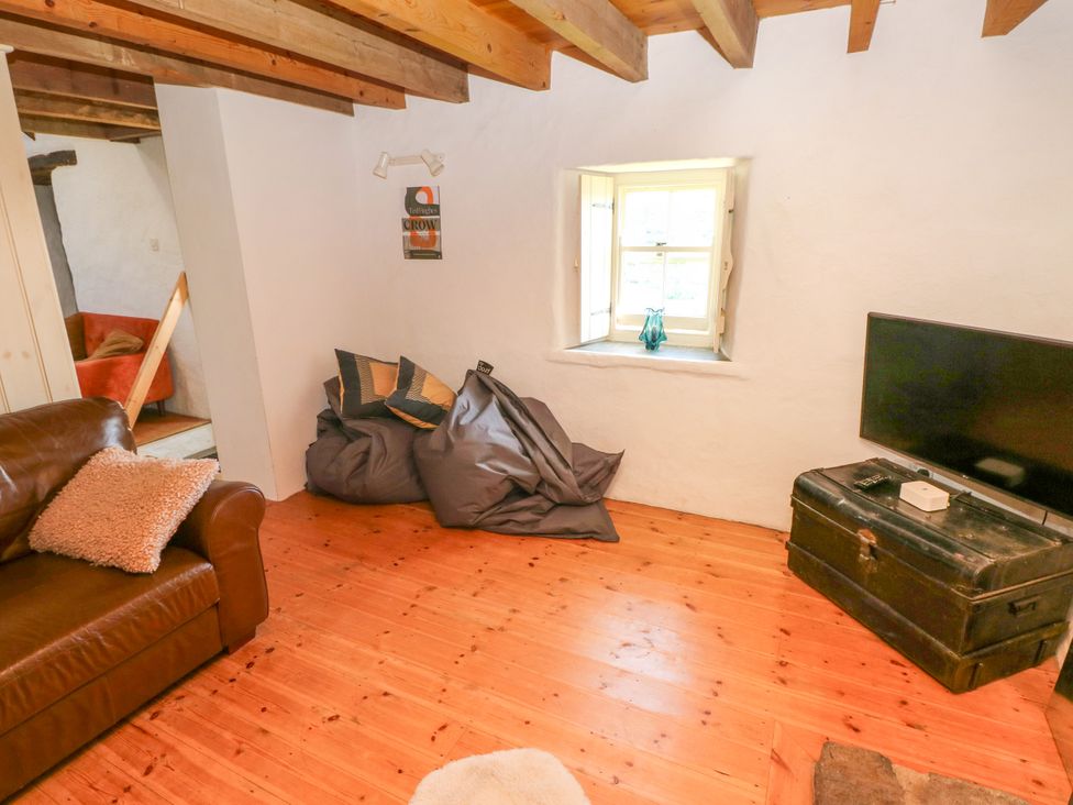 A room with wooden floor beams a leather sofa bean bags a window and a television on a chest at Ty Mellen in Dinas Cross