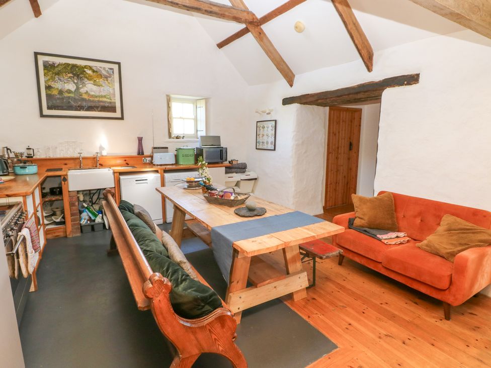 A kitchen and dining area with wooden beams a wooden table benches an orange sofa and kitchen appliances at Ty Mellen in Dinas Cross