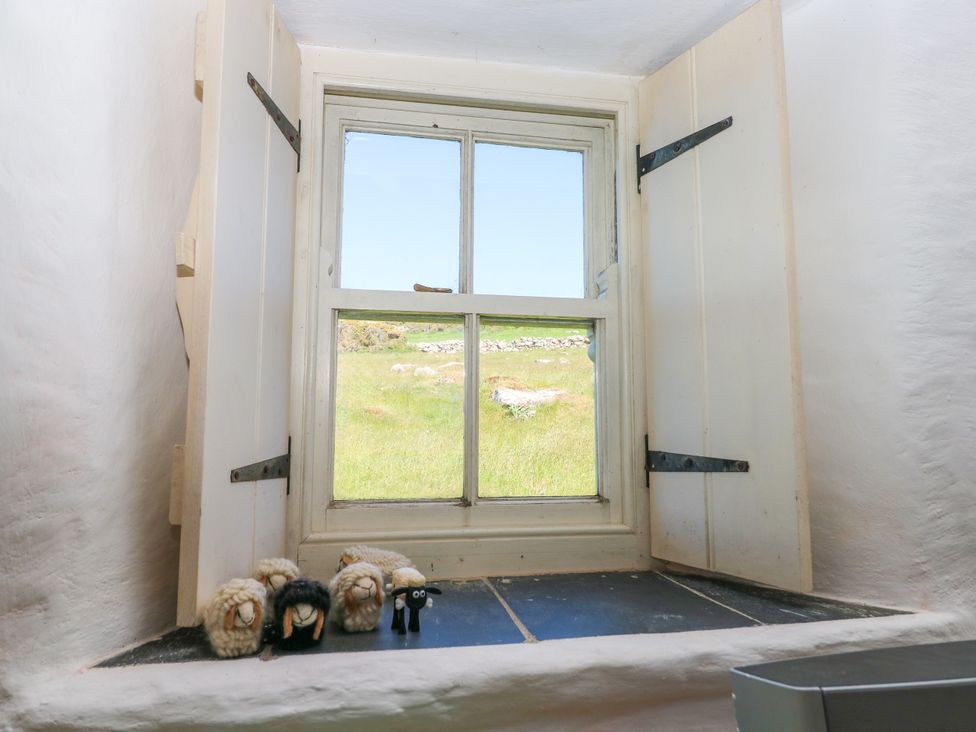 A window with open shutters looking out to a grassy field with rocks and small wool sheep figurines on the windowsill at Ty Mellen in Dinas Cross