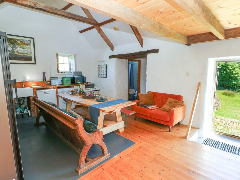 A kitchen and dining area with wooden table benches and an orange sofa at Ty Mellen in Dinas Cross