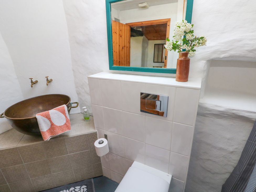 A bathroom with a copper basin sink a towel on the basin a toilet with a tiled wall and a large mirror with a vase of flowers on top at Ty Mellen in Dinas Cross