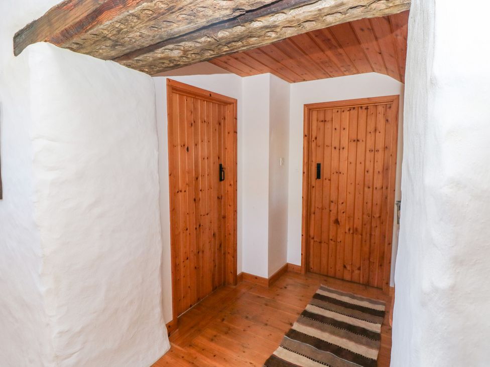 A hallway with wooden doors wooden floor a rug and white textured walls at Ty Mellen in Dinas Cross