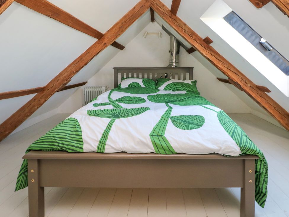 A bedroom with a bed featuring green leaf patterned bedding under wooden ceiling beams at Ty Mellen in Dinas Cross