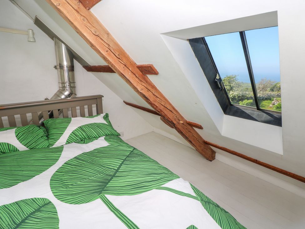 A bedroom with a bed near a slanted ceiling wooden beam and a skylight window showing an outdoor view at Ty Mellen in Dinas Cross