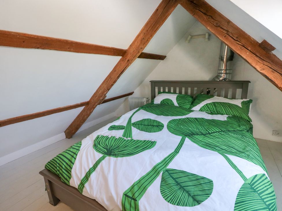 A bedroom with a bed with green leaf patterned bedding and wooden beams on the ceiling at Ty Mellen in Dinas Cross