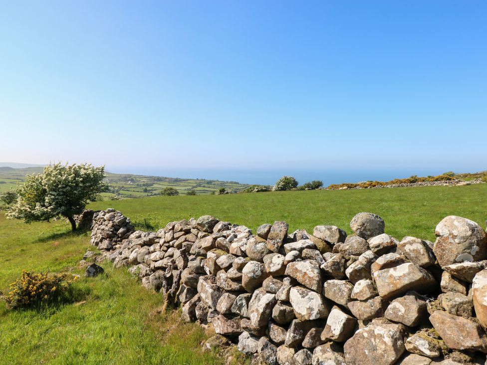 A stone wall running through green fields with a tree and distant hills under a clear blue sky at Ty Mellen in Dinas Cross