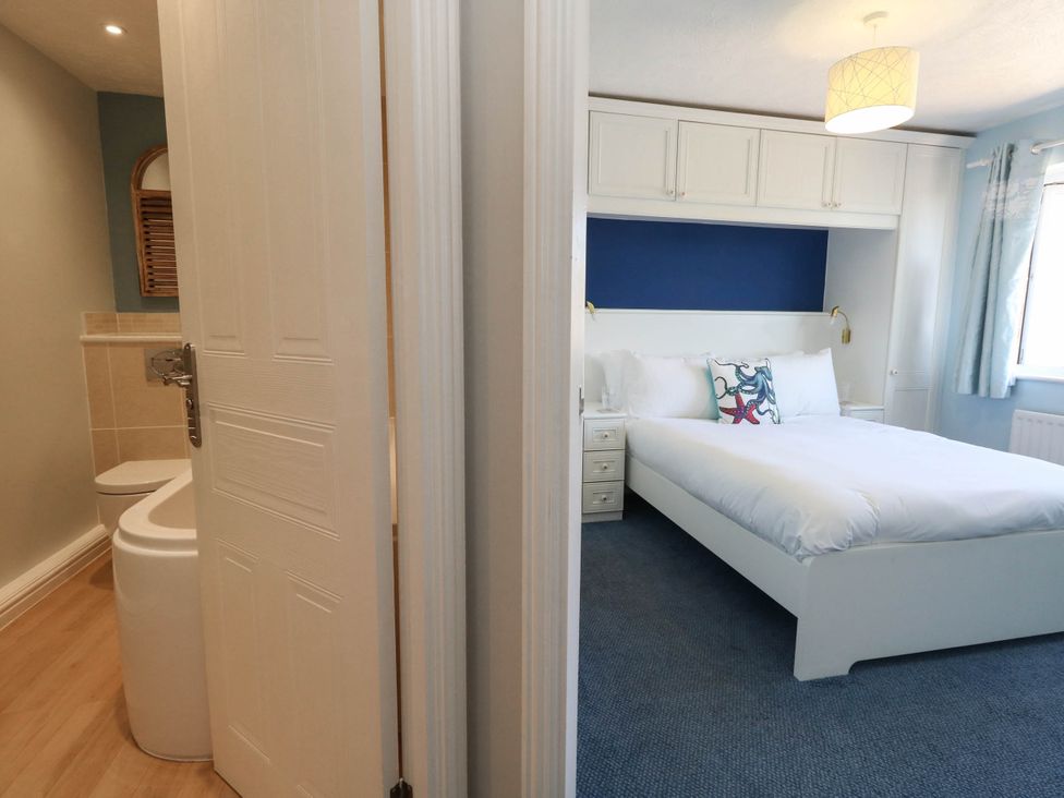 A bathroom with a toilet and sink beside a bedroom with a bed at Cove Cottage in Weymouth