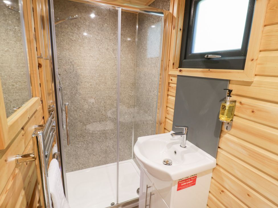 A bathroom with a shower and sink at The Shepherds Hut at Bridge Lake Farm & Fishery Chacombe