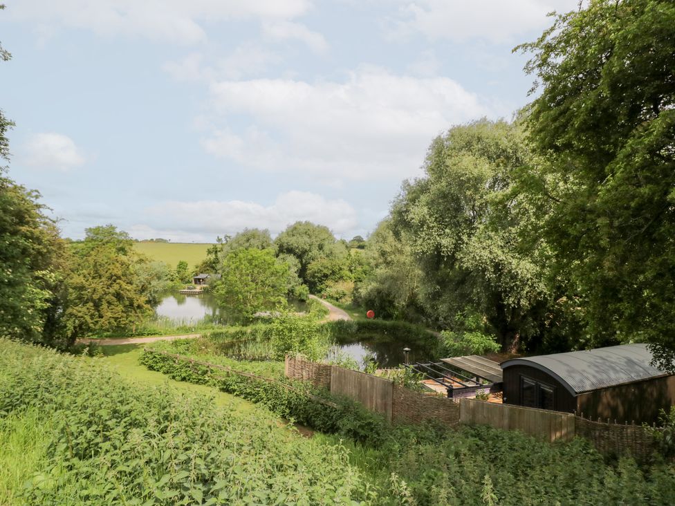 An outdoor area with trees and a water body at The Shepherds Hut at Bridge Lake Farm & Fishery Chacombe
