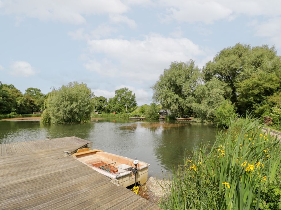 A lake with a boat on a dock at The Shepherds Hut at Bridge Lake Farm & Fishery Chacombe