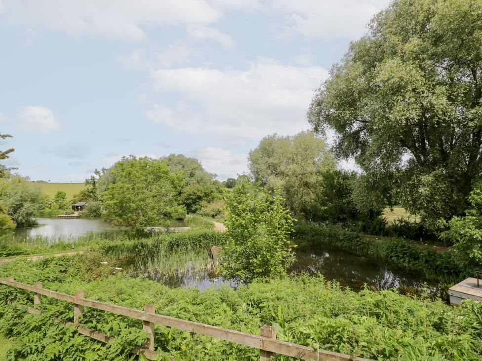 A scenic view of a pond surrounded by trees and grass at The Shepherds Hut at Bridge Lake Farm & Fishery Chacombe