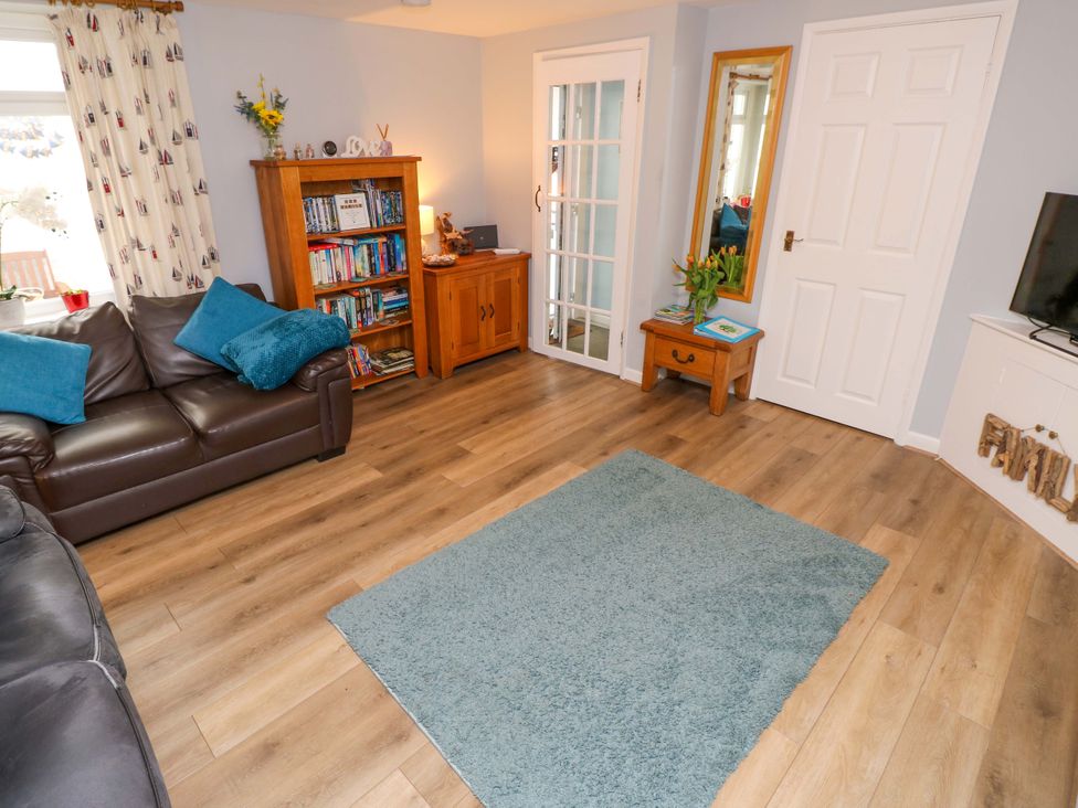 A living room with a sofa, bookshelf, and television at Willow Cottage in Ventnor
