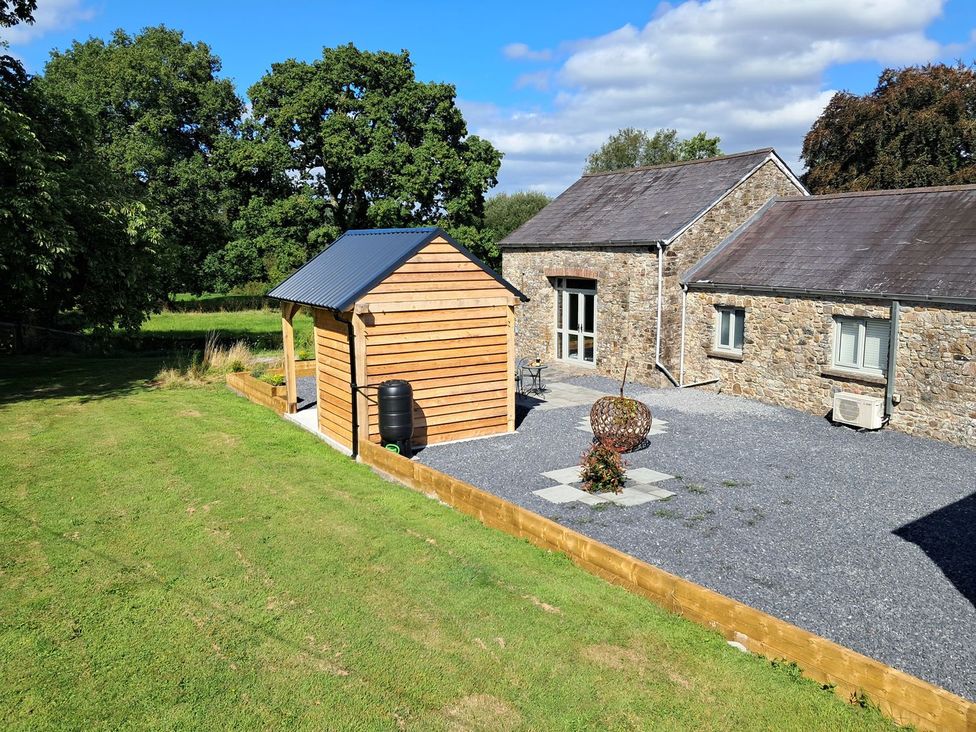A garden with a wooden shed and stone building at Dinefwr Cottage Golden Grove near Llandeilo