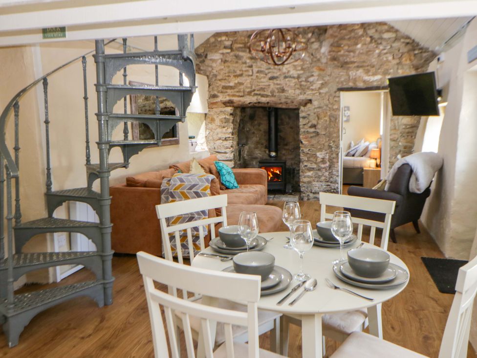 A living room with a spiral staircase and dining area at Cobwebs near Cold Inn near Saundersfoot
