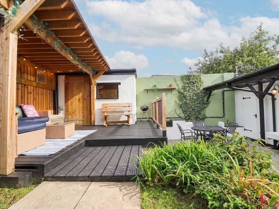 A garden with a deck, table, chairs, and plants at 18 Church Street, Llangollen