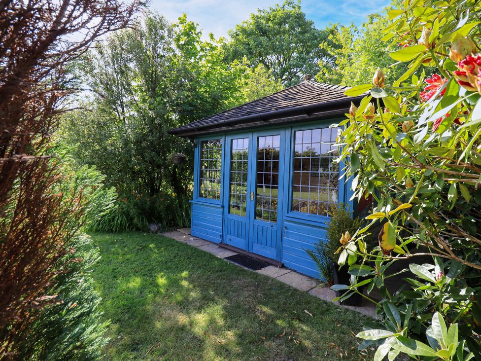 A blue shed with windows and plants in the garden at The Garden Suite at Fiddler Hall Barn, Newby Bridge