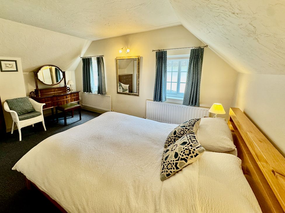 A bedroom with a bed, dressing table and window at Cajun Cottage in West Lulworth