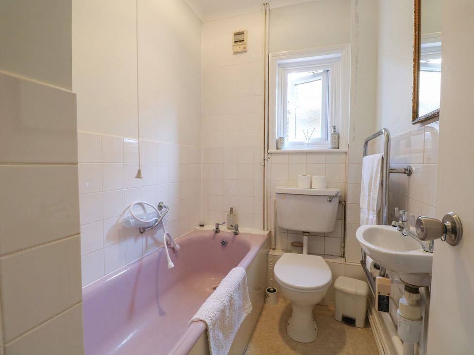 A bathroom with pink bathtub, toilet and sink at Sylvian in Bexhill-On-Sea