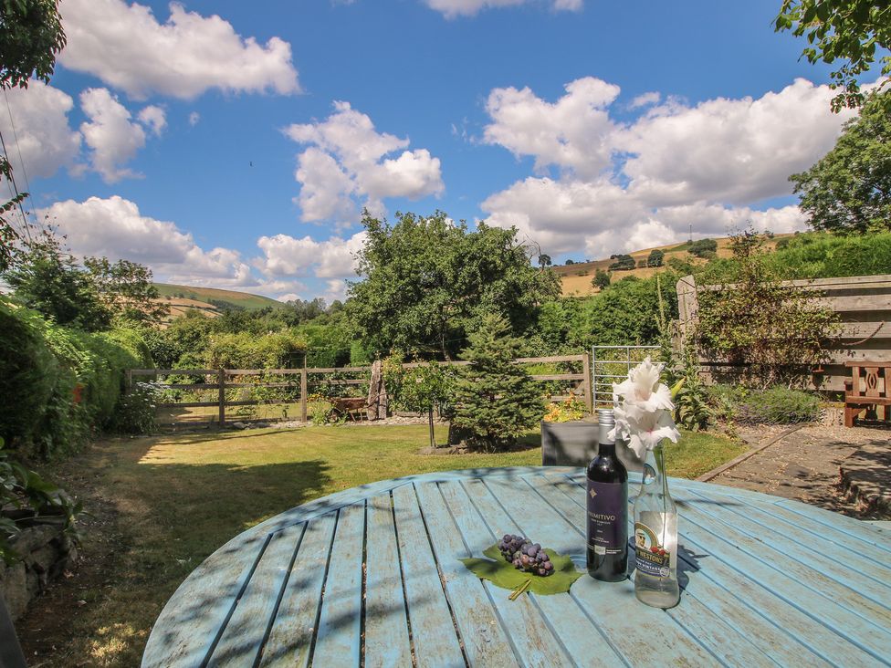 A garden with a blue table and wine bottles at Buzzards Breg in Builth Wells