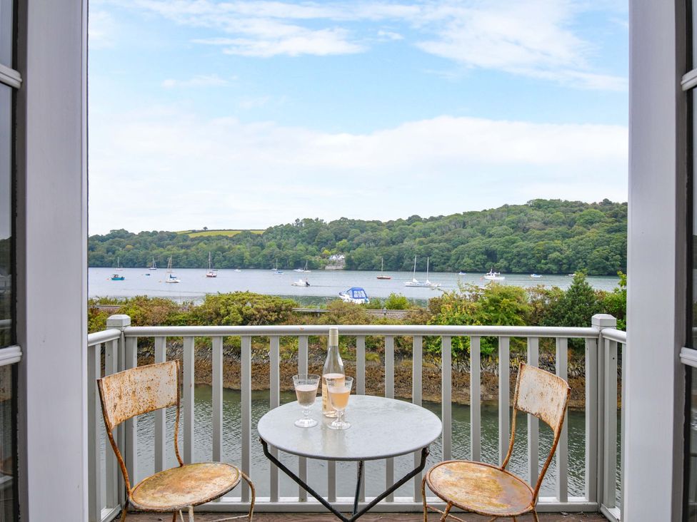 A balcony with chairs and a table overlooking a waterfront at Island House in Golant near Tywardreath