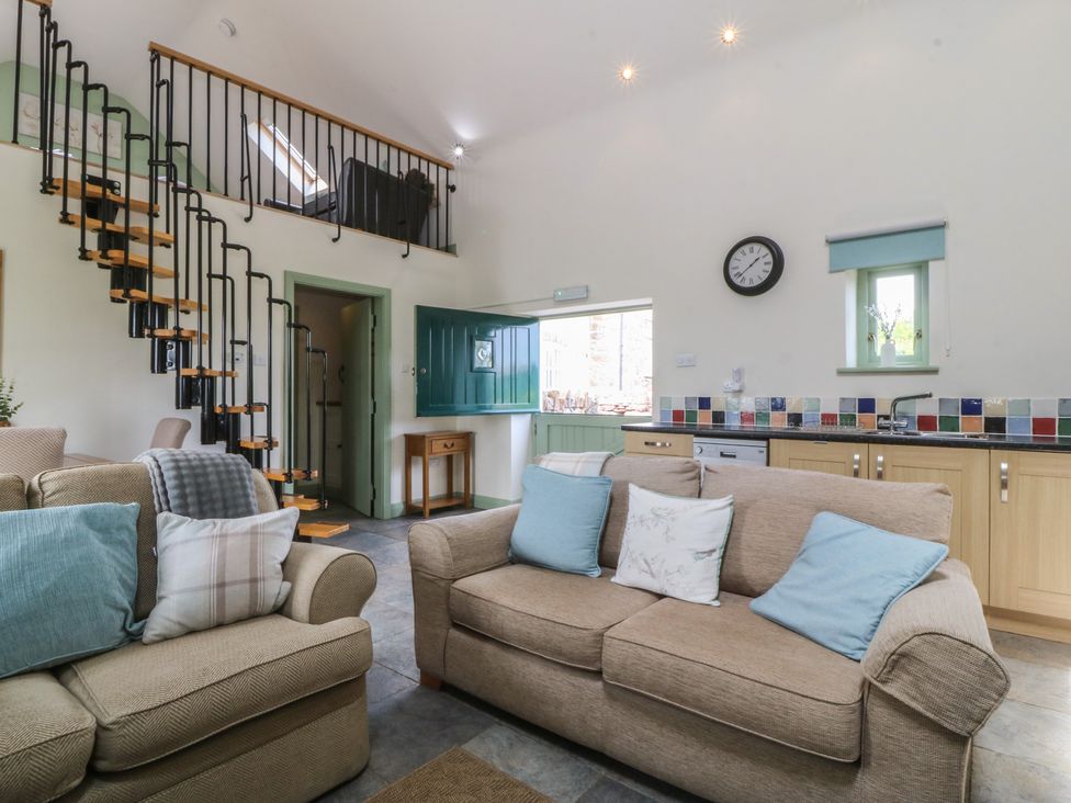A living room with a sofa, armchair, and staircase at No 1 The Granary, Capel Coch near Llannerch-Y-Medd