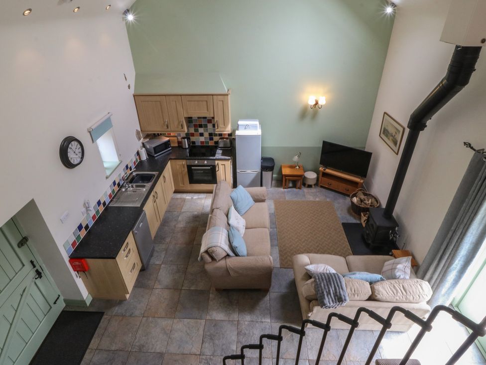 A living room with a sofa, TV, and kitchen area at No 1 The Granary, Capel Coch near Llannerch-Y-Medd