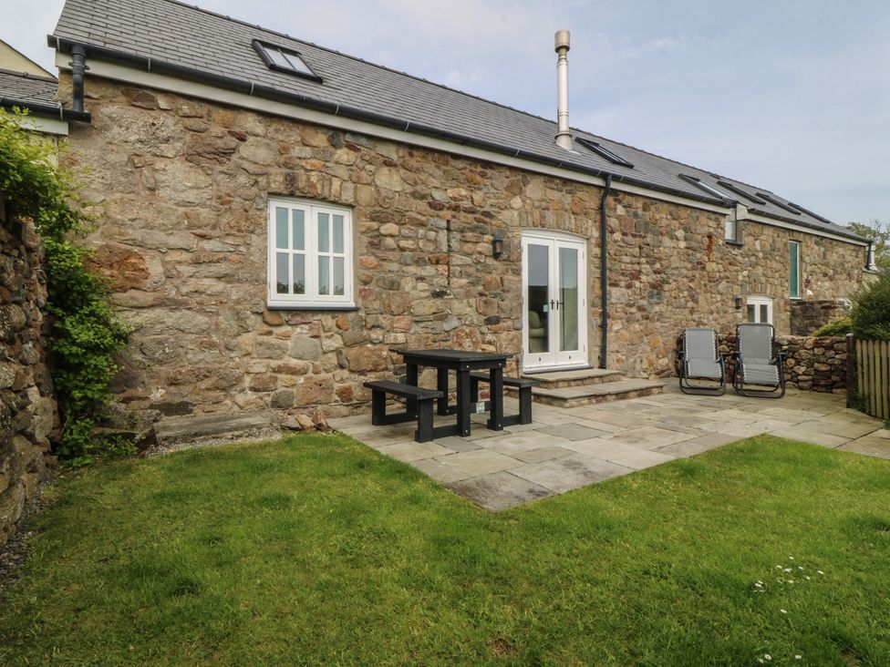 An outdoor patio with a stone wall and garden furniture at No 1 The Granary in Capel Coch near Llannerch-Y-Medd