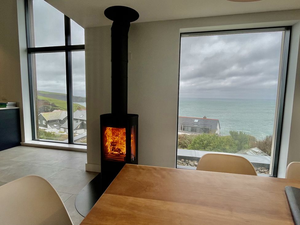 A dining room with a wood stove and large windows showing the coastline at The Old Coastguard Lookout Port Isaac