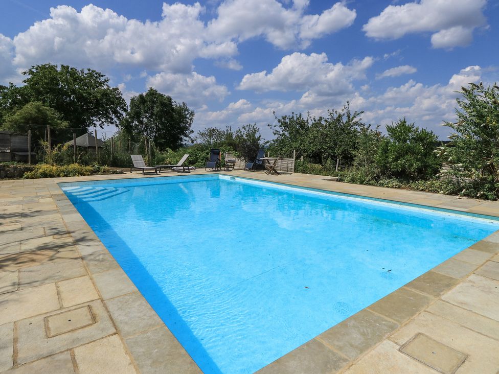 A swimming pool surrounded by sun loungers and plants at Byre Cottage 4, Sullington near Storrington