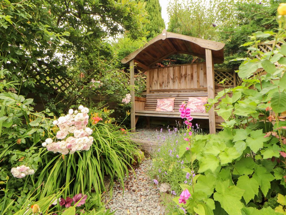 A garden with a wooden seat surrounded by plants and flowers at West View in Leasgill near Milnthorpe