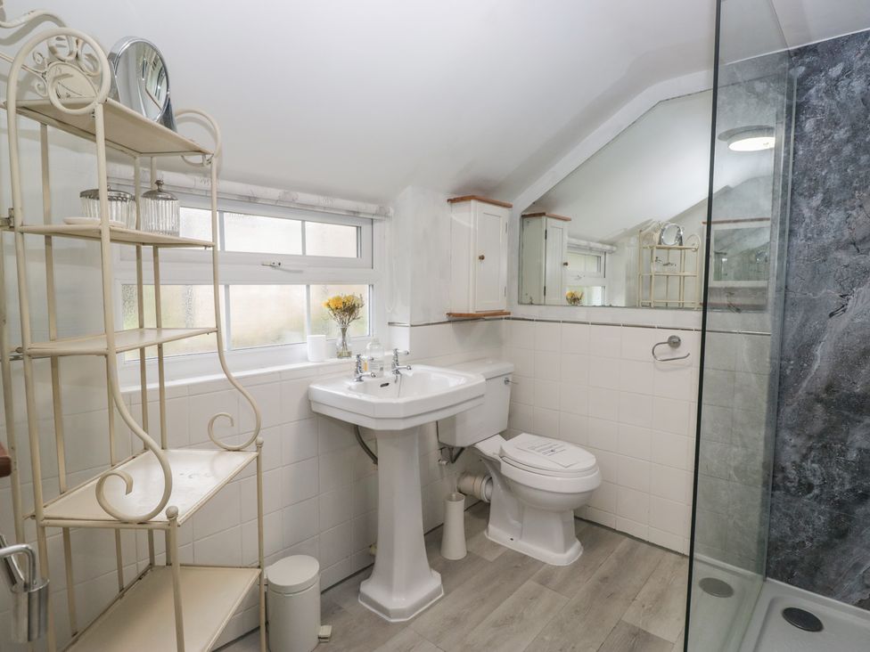 A bathroom with a sink, toilet, shower, and shelf at Bay Tree Cottage in Ambleside