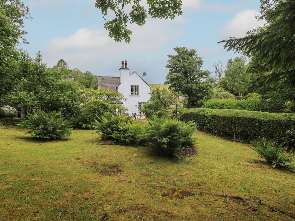 A garden with a house and trees at The Old Post House at Low Stott Park near Newby Bridge