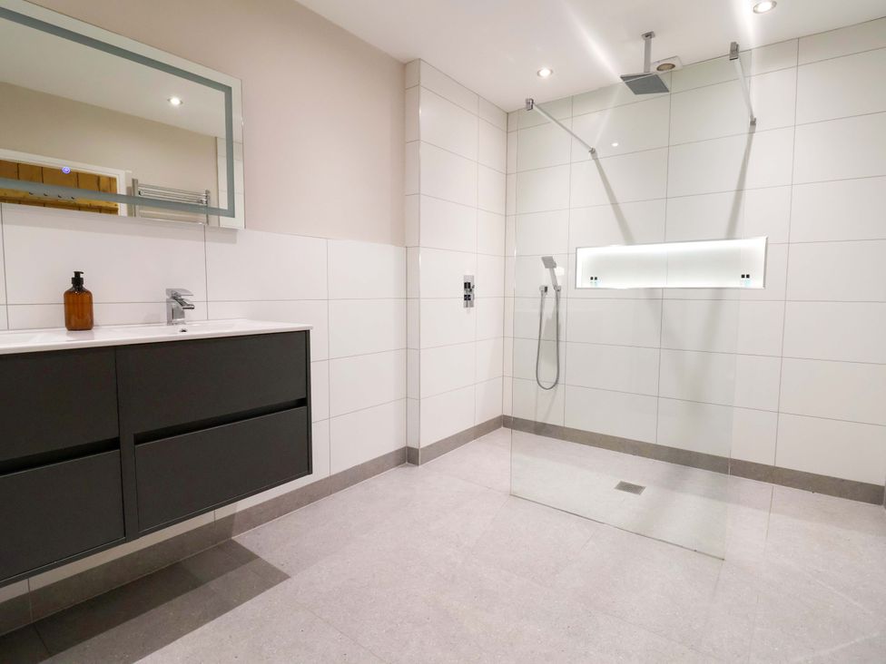 A bathroom with a shower, vanity unit and mirror at Carriage House Capesthorne near Chelford