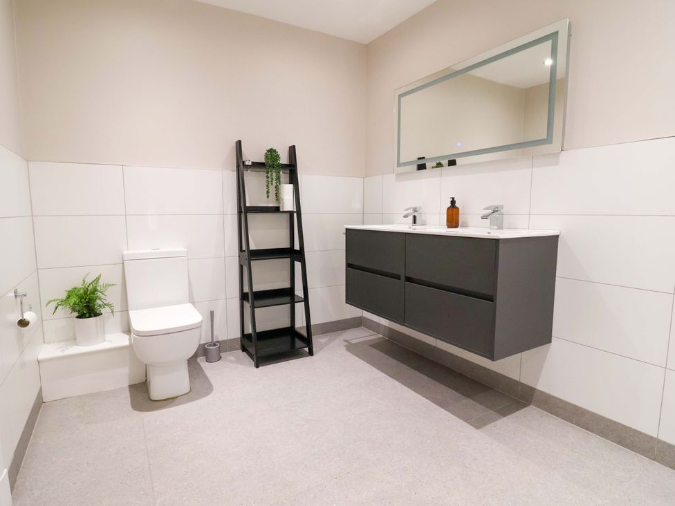 A bathroom with a toilet, sink, mirror, and shelf at Carriage House in Capesthorne near Chelford