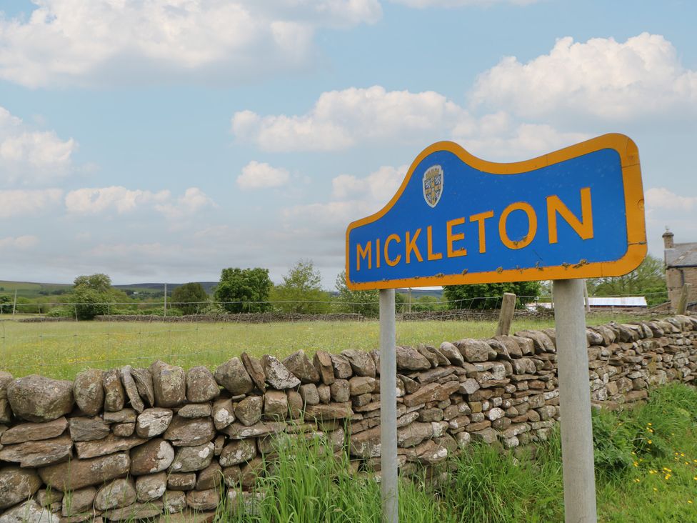 A sign for Mickleton near a stone wall in a rural area