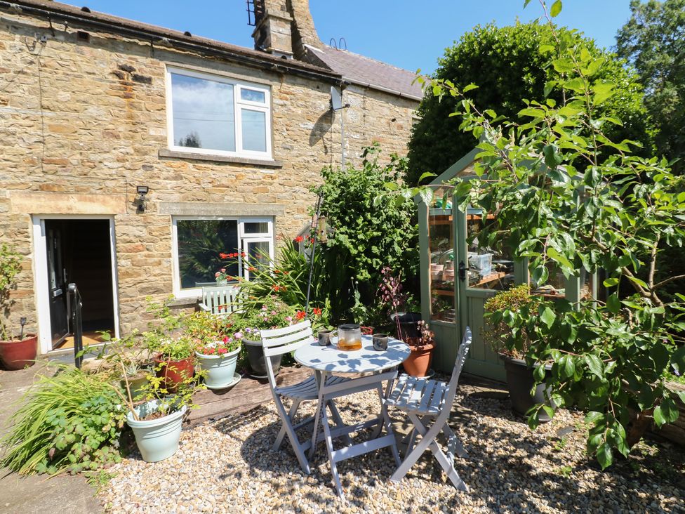A garden with a table and chairs near a greenhouse at Banklands in Mickleton, Teesdale