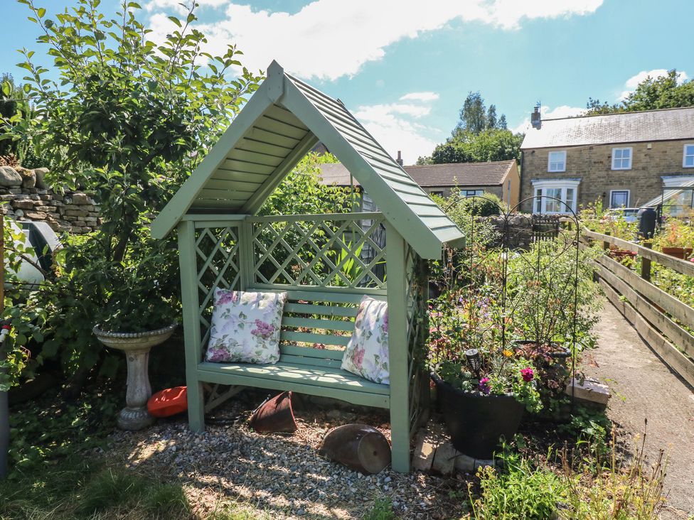 A garden with a green bench and birdbath at Banklands Mickleton, Teesdale