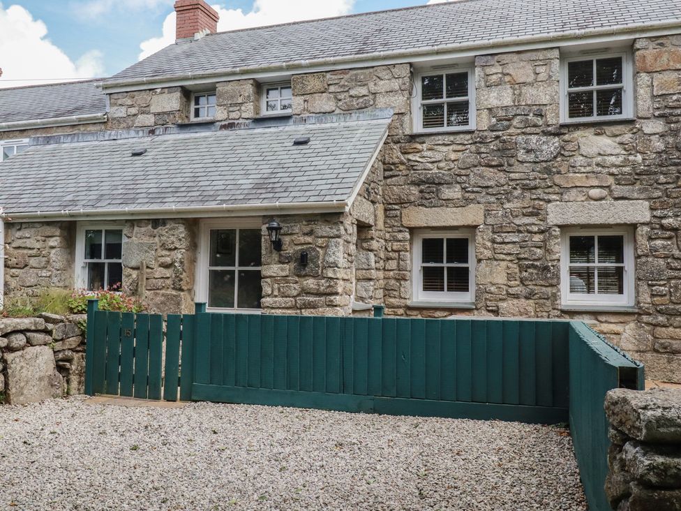 A stone house with windows and a green fence at 15 Boscaswell Downs in Pendeen