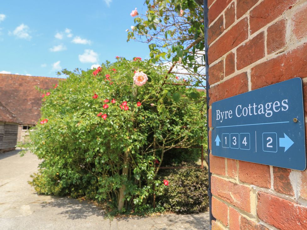 A sign for Byre Cottages with flowers and a building in Sullington near Storrington