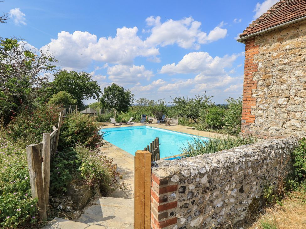An outdoor swimming pool with deck chairs and a stone wall at Byre Cottage 3 Sullington near Storrington