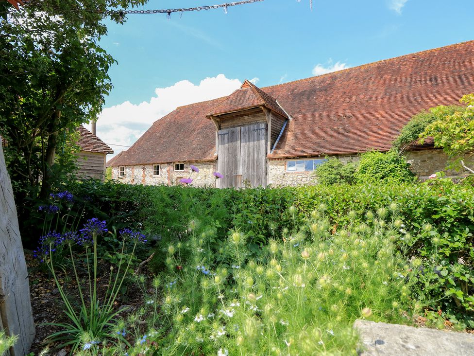A garden with flowers and a barn in the background at Byre Cottage 2 Sullington near Storrington