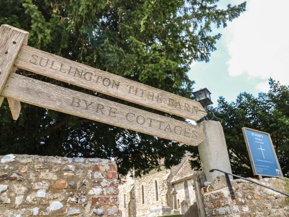 A wooden sign pointing to Sullington Tithe Barn and Byre Cottages near St Mary's in Sullington near Storrington